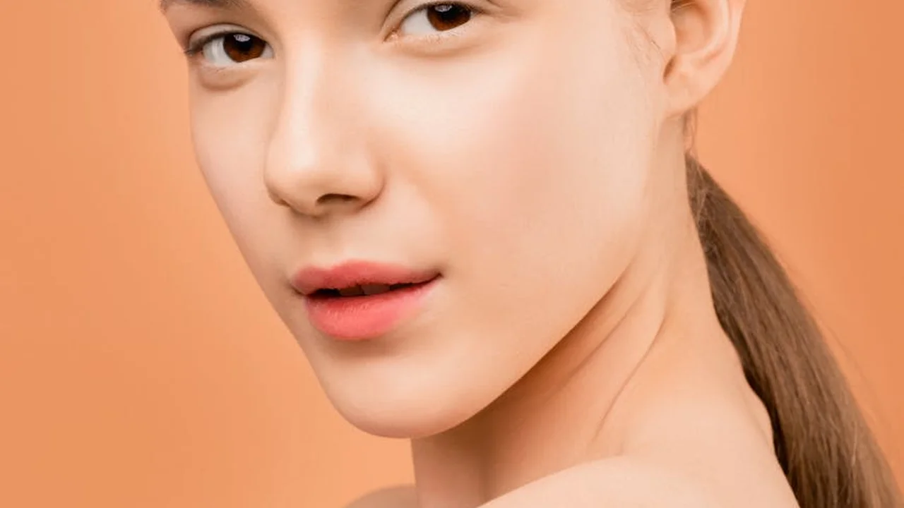 Close-up portrait of a person with smooth, even skin against a peach background