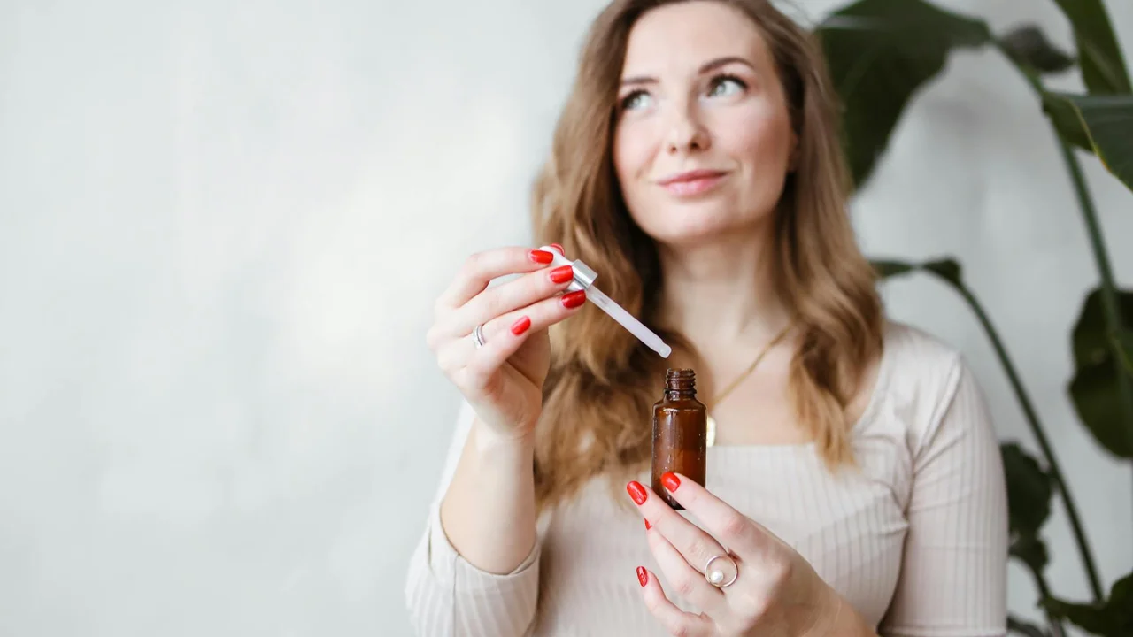 A woman holding a dropper bottle of oil, preparing to apply it to her hair.