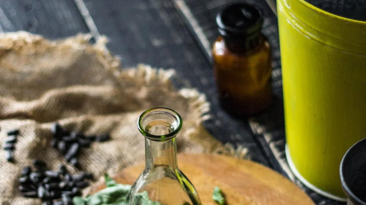 Close-up of ritual anointing oil items on a dark wooden surface: a small clear glass bottle, an amber bottle, burlap fabric, and a lime-green container.