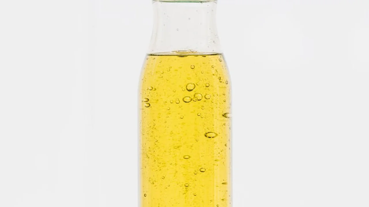 Clear glass bottle filled with golden apricot kernel oil against a white background with small bubbles.