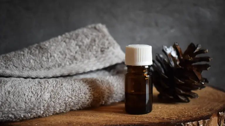 Amber glass bottle with a white cap on a wooden surface, beside a folded gray towel and a pine cone.