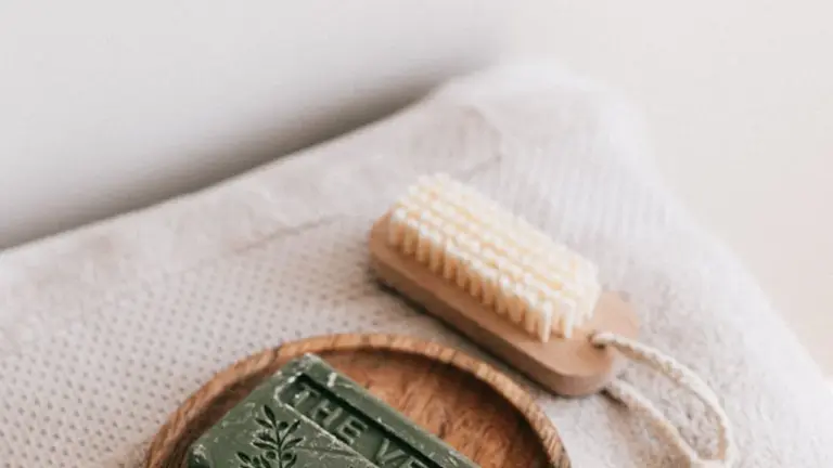 Green cleansing soap bar with partial white lettering beside a small wooden cleansing brush on a soft beige towel.