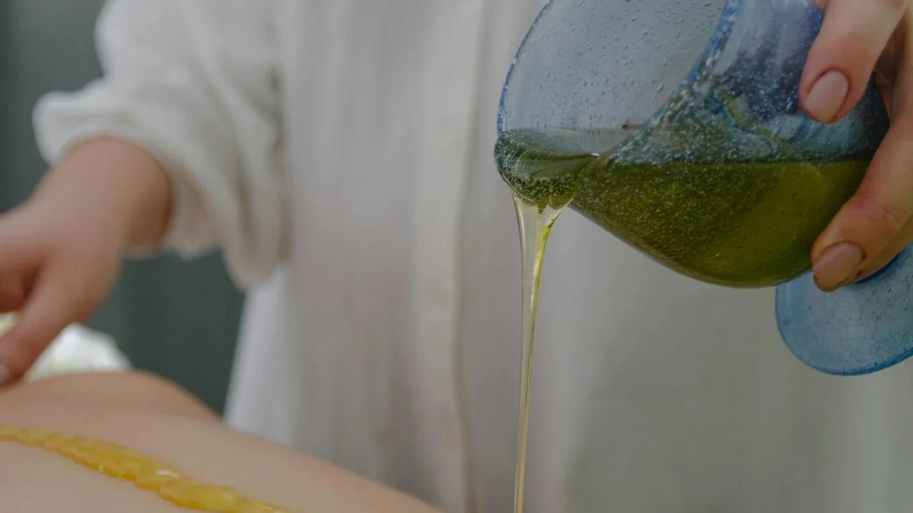 A person tilts a blue container to pour a yellow-green liquid, representing automotive oil being handled