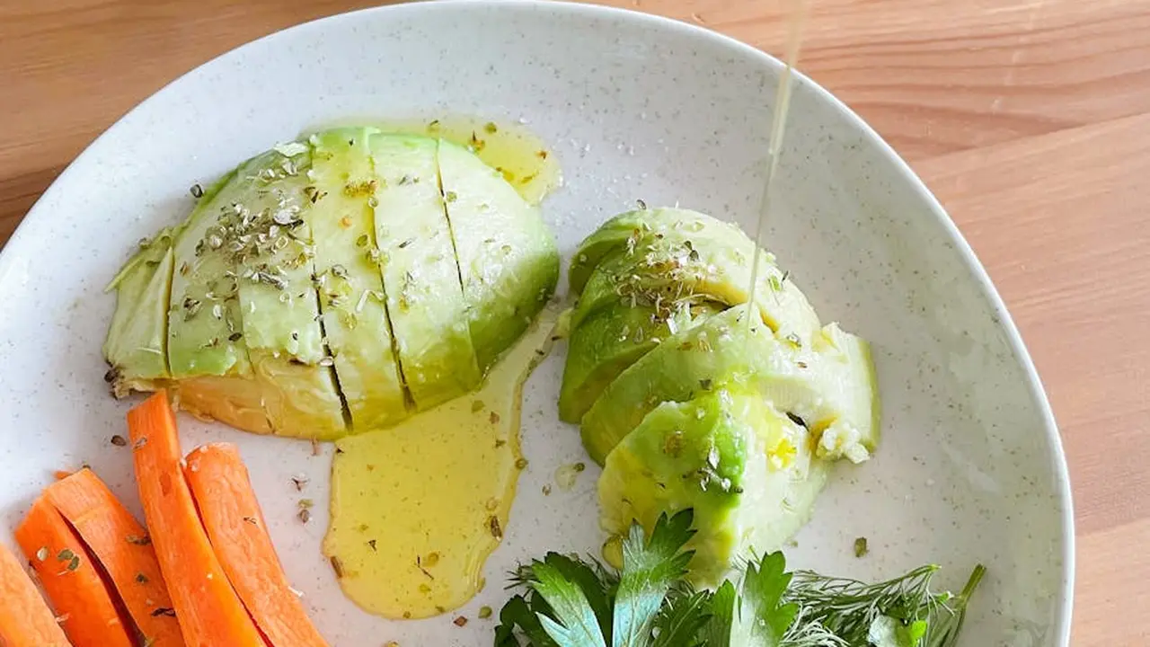Two avocado halves arranged on a light plate with oil drizzled around them and a few herbs sprinkled on top.