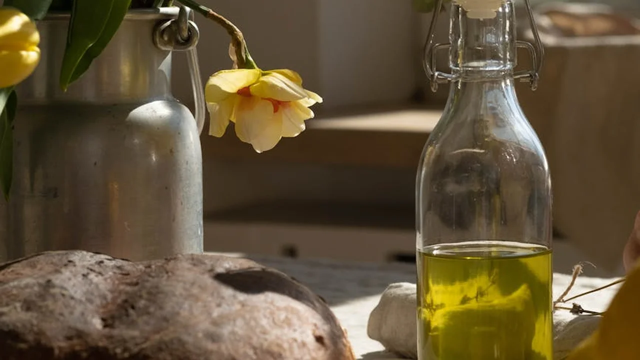 Close-up of a glass bottle filled with golden oil on a rustic surface with a flower in the background, representing avocado and olive oils for skincare.