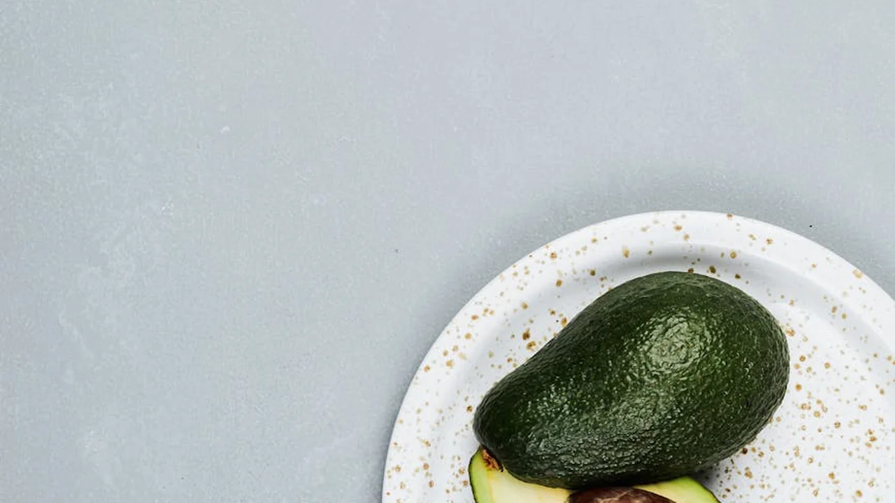 A ripe avocado on a white plate against a pale gray background.