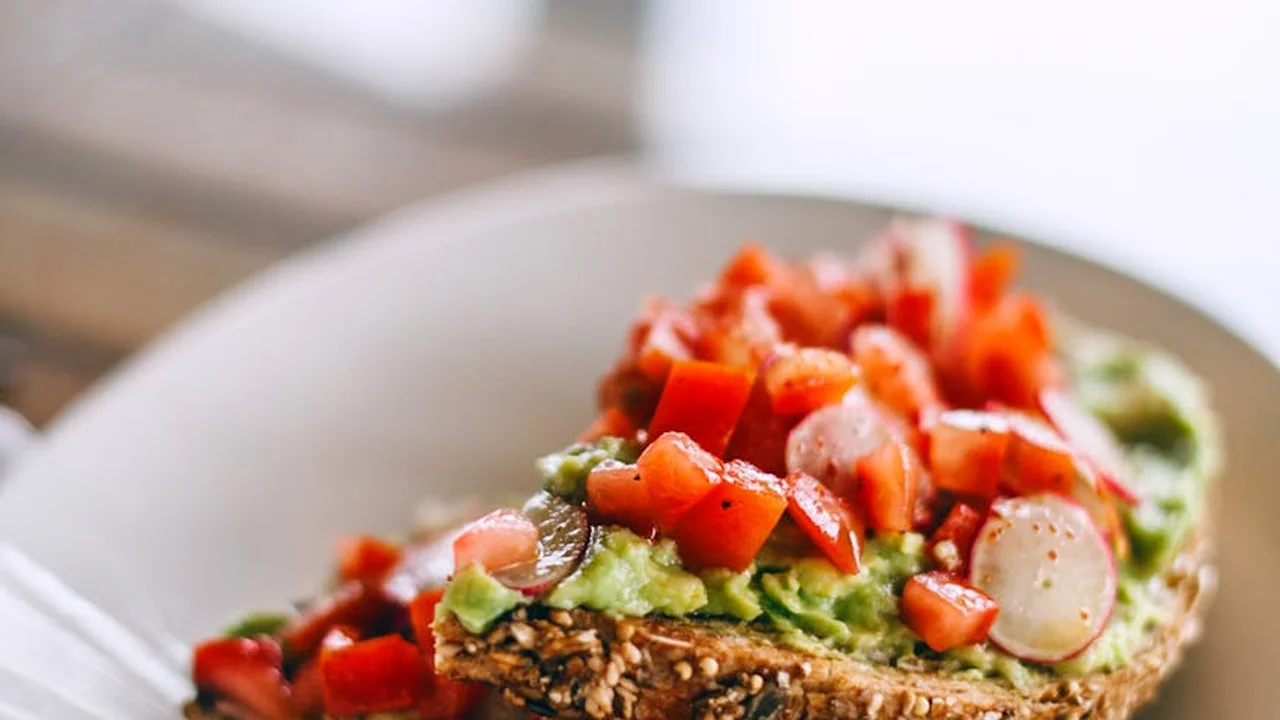 Close-up of avocado toast with mashed avocado, diced tomatoes, and radish slices on a slice of bread.