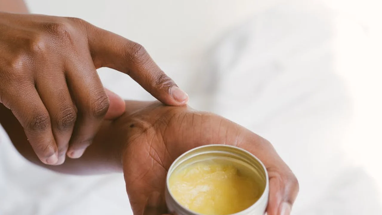 Close-up of hands with a small jar of oil, illustrating preparing to moisturize the skin with avocado oil.