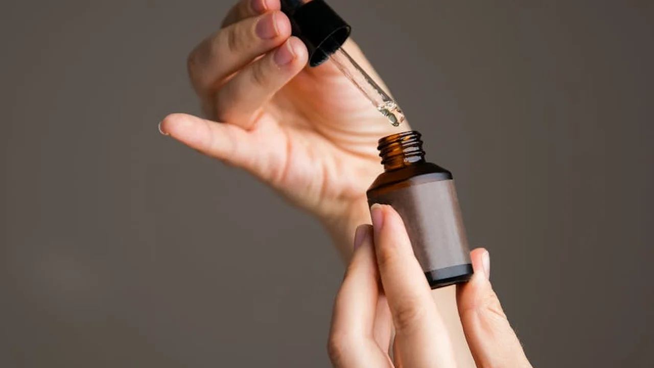 Close-up of hands holding a brown glass bottle and dropper, dispensing oil.