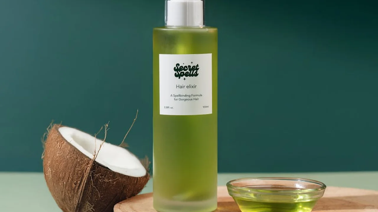 A bottle of batana oil with a halved coconut and a small bowl of oil on a green background