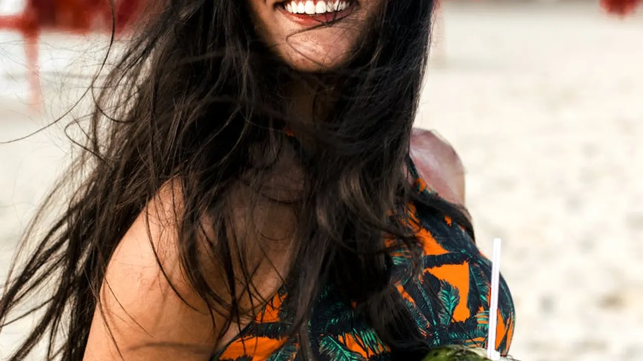 Person at the beach with wind-blown hair wearing an orange and black patterned top