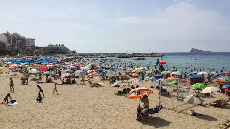 A crowded beach with colorful umbrellas, sunbathers, and people near the shoreline.