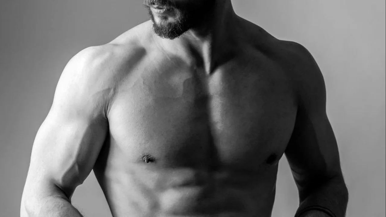 Grayscale image of a muscular, shirtless man with a trimmed beard