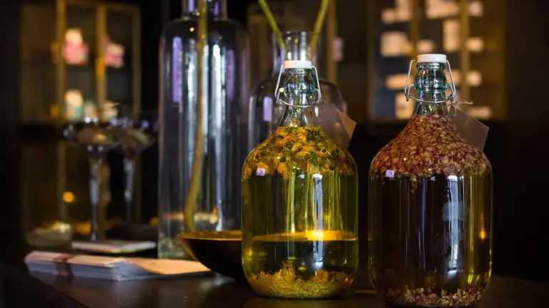 Glass bottles of oil on a wooden counter in a shop, with one bottle containing seeds.