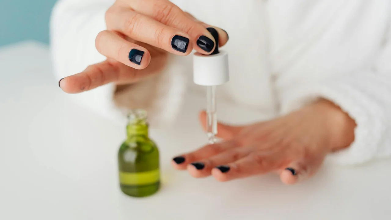 Close-up of a hand holding a dropper over a small bottle of oil, with a second bottle in the background.