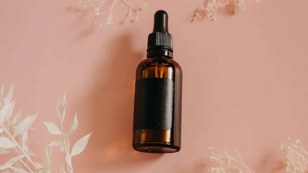 Brown glass dropper bottle with a black label on a soft pink background, representing antioxidant-rich botanical oils used in skincare.