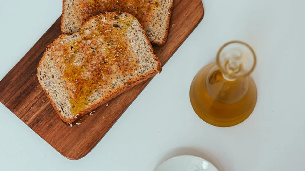 Sliced bread on a wooden cutting board with a small bottle of oil on a pale blue background