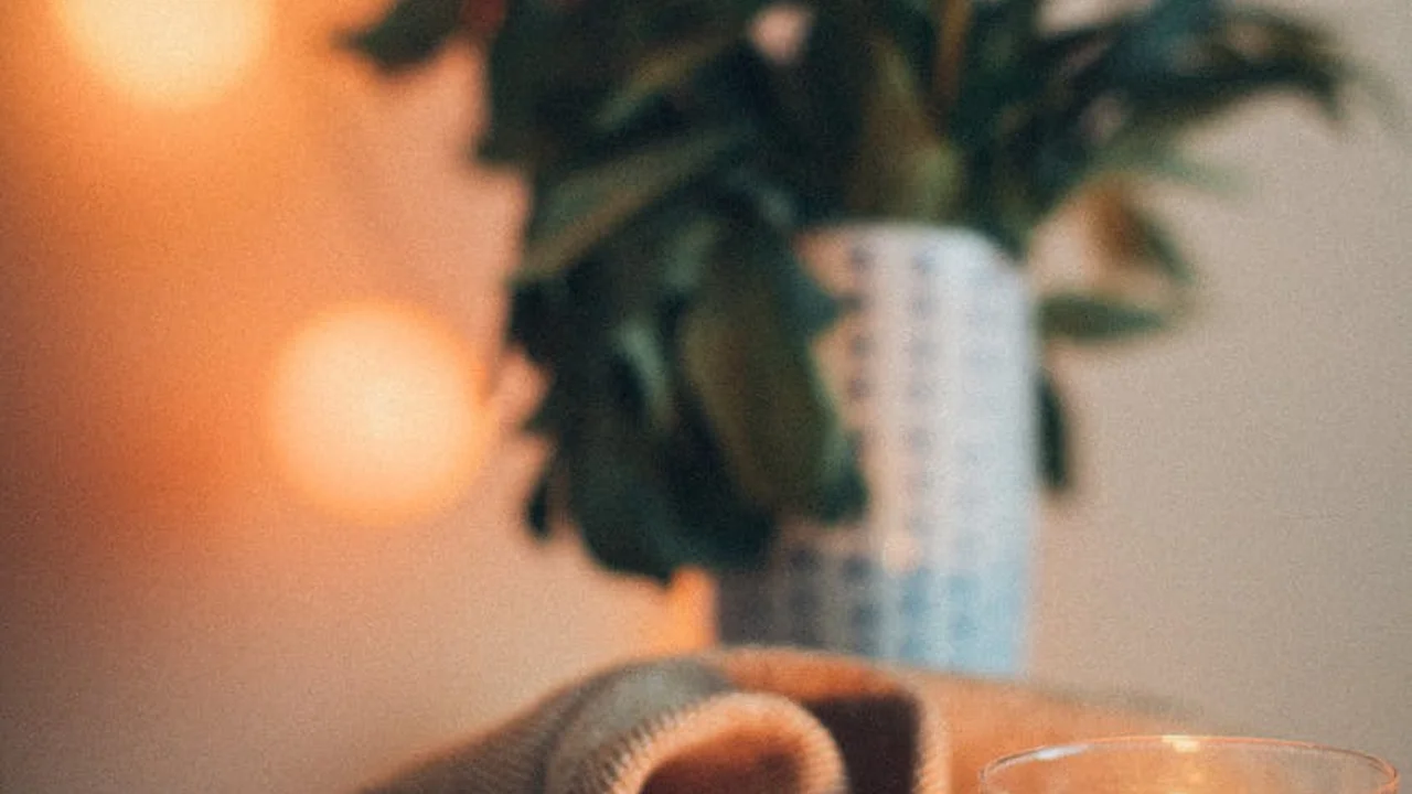 Close-up of a candle jar with a warm glow and a blurred plant in the background.