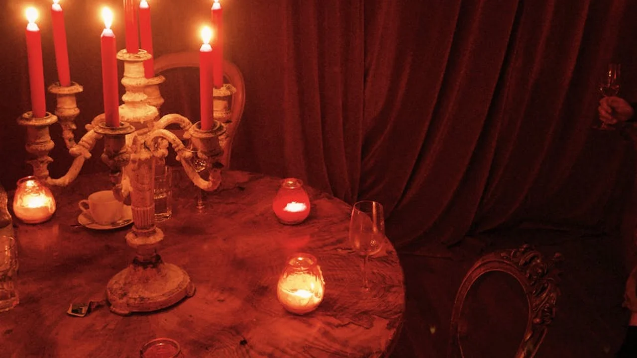 Dim candlelit scene with a decorative candelabrum and small candles on a table in front of red drapes, creating a cozy spa-like atmosphere.