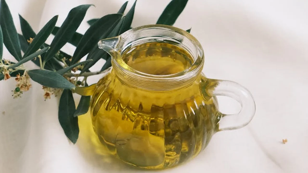 Glass jug of golden herbal-infused oil with green leaves on a light background.