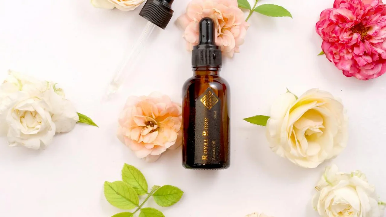 Brown glass dropper bottle of carrier oil surrounded by pastel roses on a clean light background