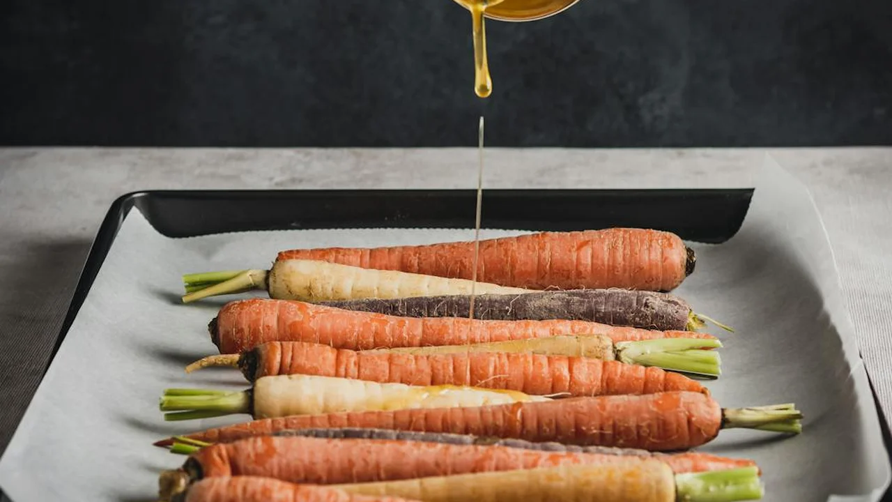 Carrots arranged on a parchment-lined baking sheet as oil is drizzled from above.