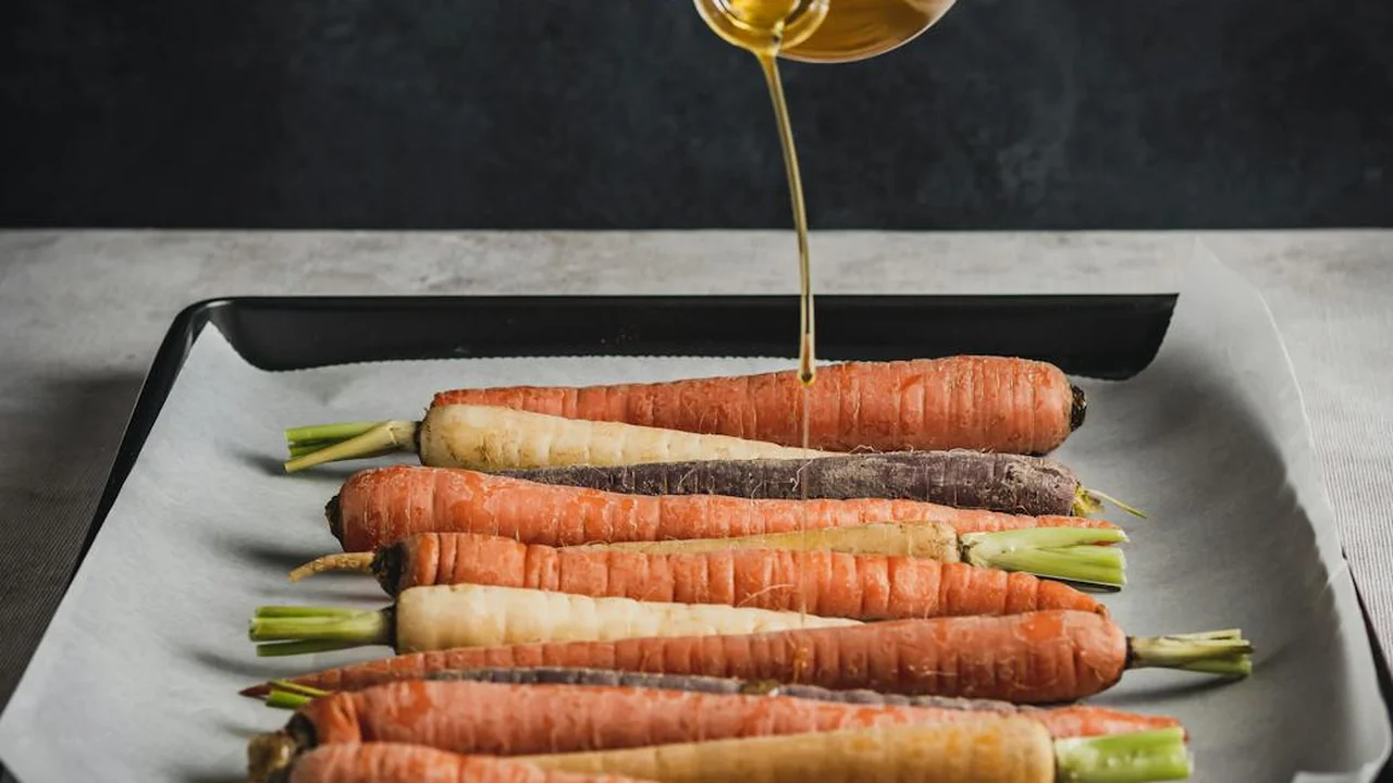 Carrots arranged on a parchment-lined baking sheet with oil being poured over them.