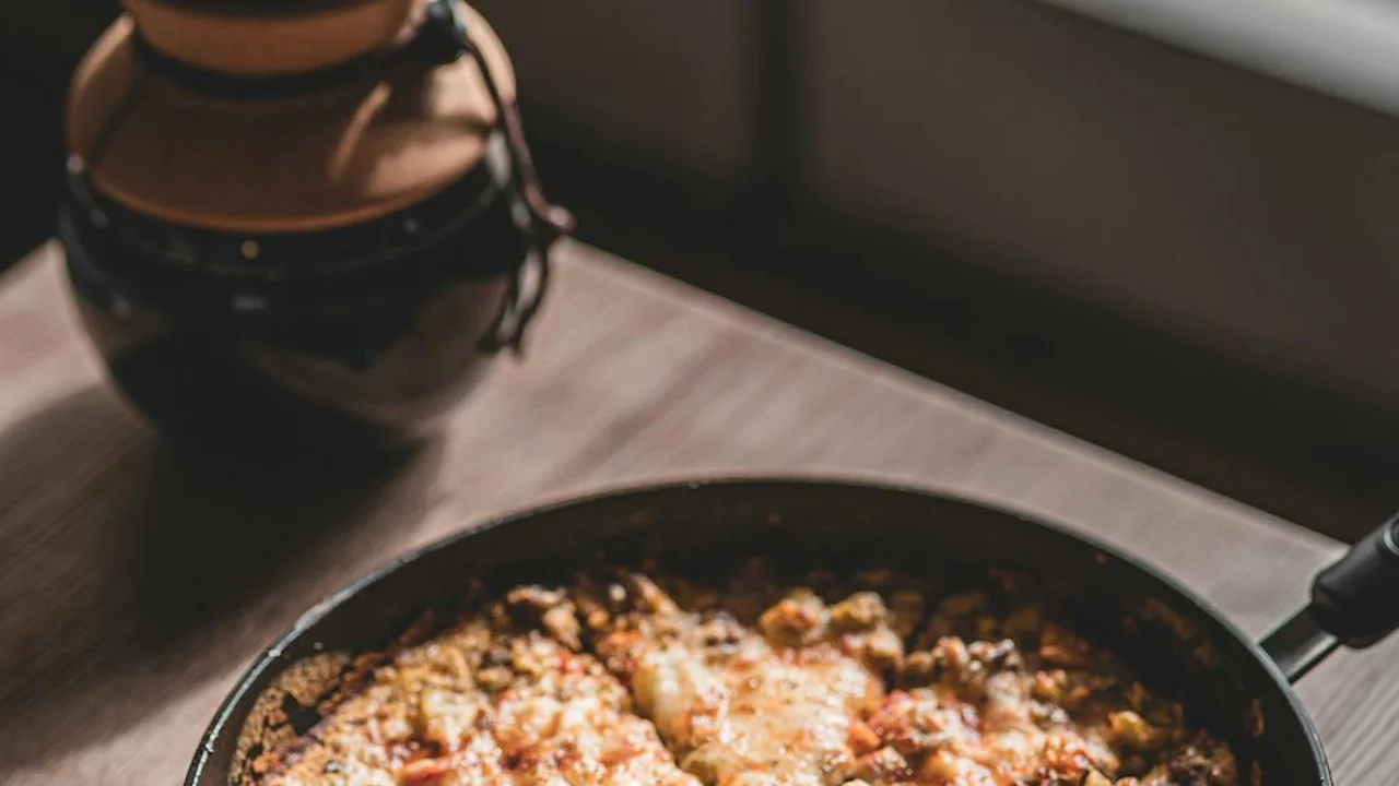 Cast iron skillet with a cooked dish on a wooden surface, and a jar of cooking oil in the blurred background.