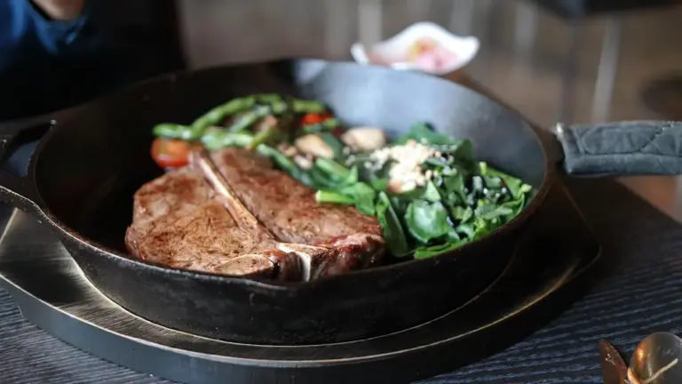 Cast iron skillet with steak and greens on a dark wooden table