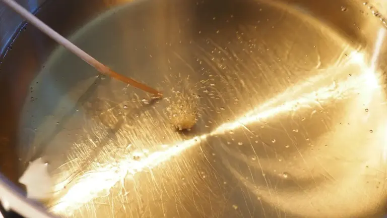 Close-up of a stainless steel bowl containing pale castor oil with a dropper resting on the rim.