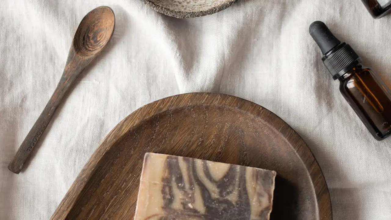 A rustic setup with a dropper bottle of castor oil, a wooden spoon, and a round wooden plate on white fabric
