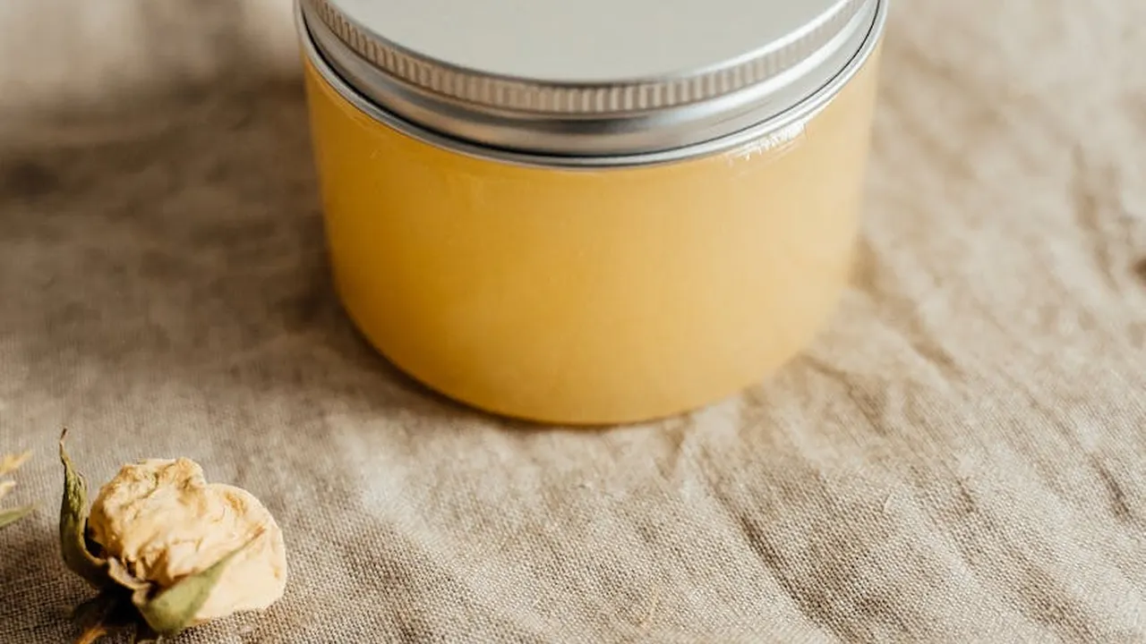 A jar of golden castor oil on a textured linen surface with a dried plant nearby