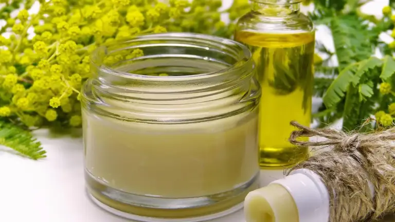 Two glass containers—one with pale castor oil and one with golden helichrysum oil—sit among fresh yellow flowers, suggesting skin-care applications.