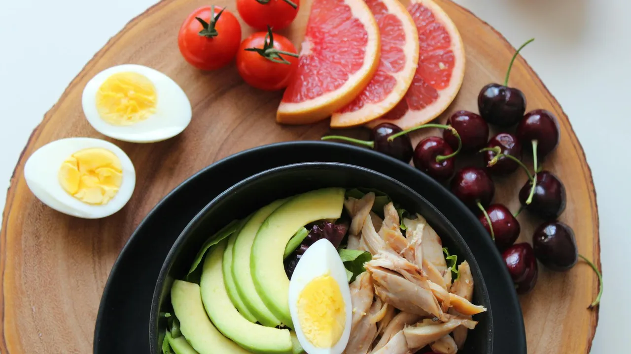 Wooden board with avocado slices arranged on a black plate, halved boiled eggs, cherry tomatoes, grapefruit wedges, and dark grapes
