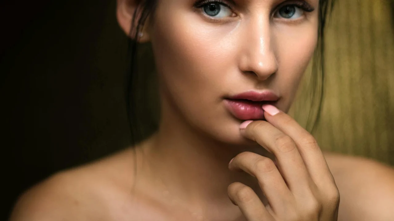 Close-up portrait of a woman with smooth skin, gently touching her lips with her fingers.