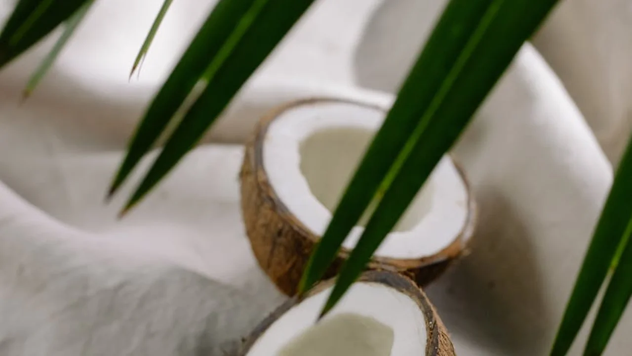 Fresh coconut halves with green leaves in the background.