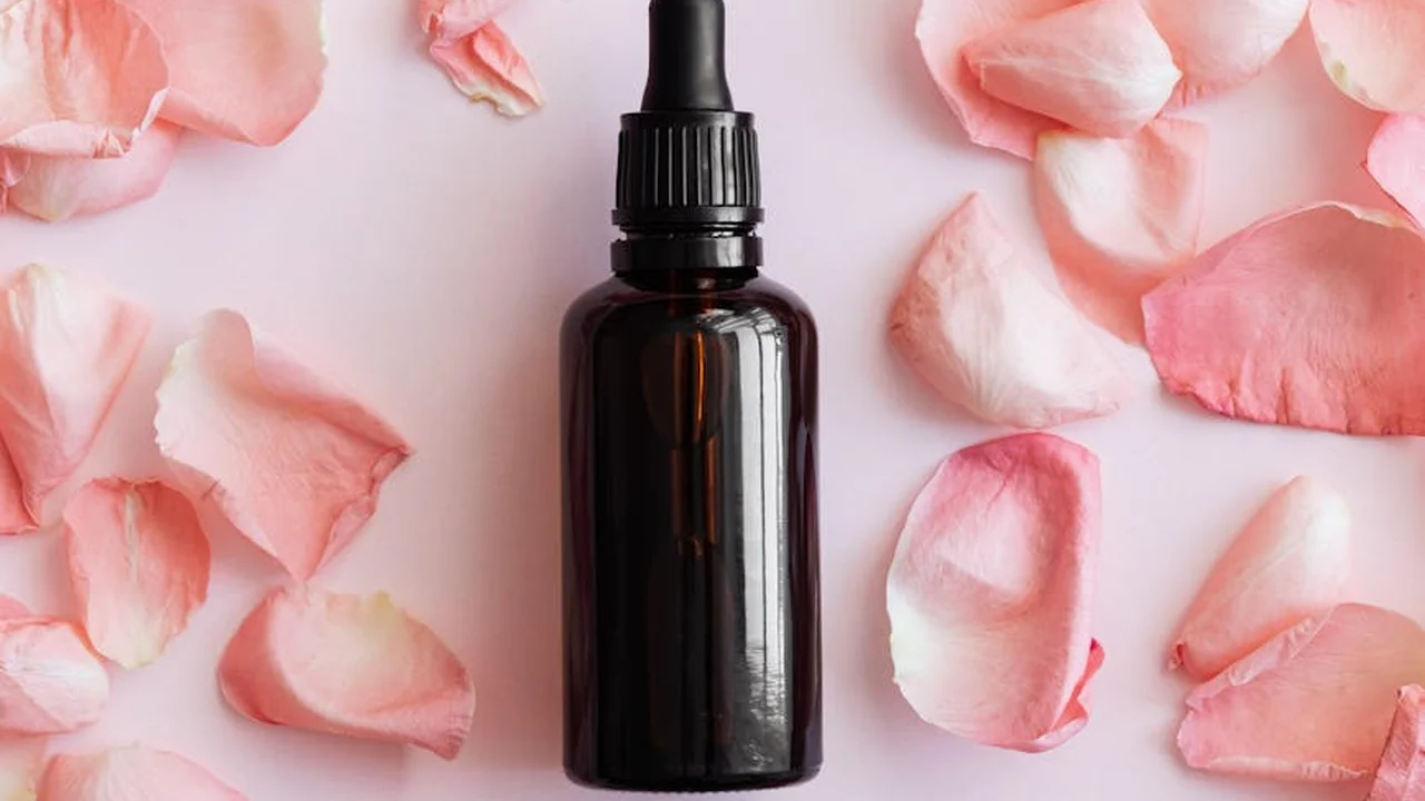 Dark glass dropper bottle surrounded by pink rose petals on a soft pink background