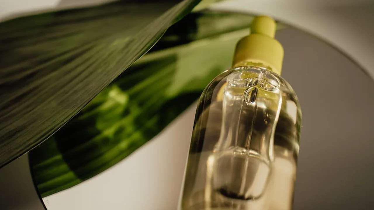Clear glass oil bottle with a yellow dropper cap and a green leaf in the background.