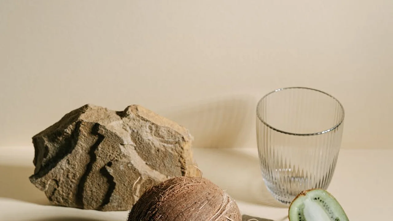 Still-life with a rough rock, a clear ribbed glass, and a slice of kiwi on a light surface