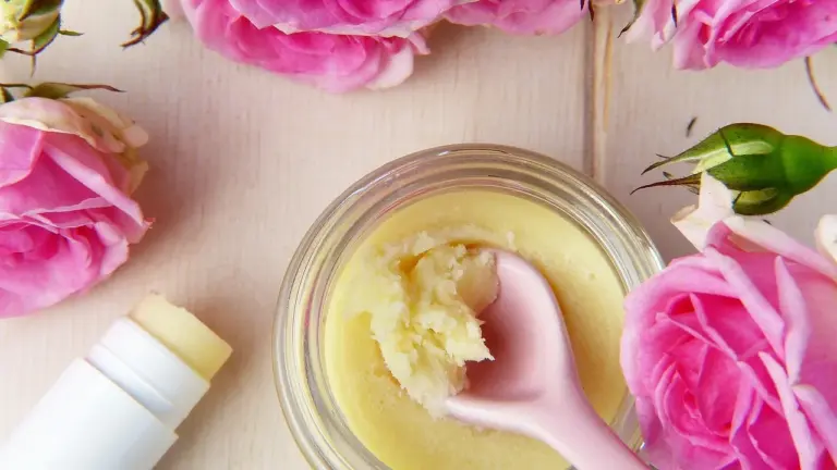 Jar of coconut oil with a pink spatula on a wooden surface, surrounded by pink roses.
