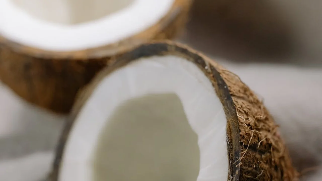 Close-up of a halved coconut showing white flesh and brown husk on a neutral surface.