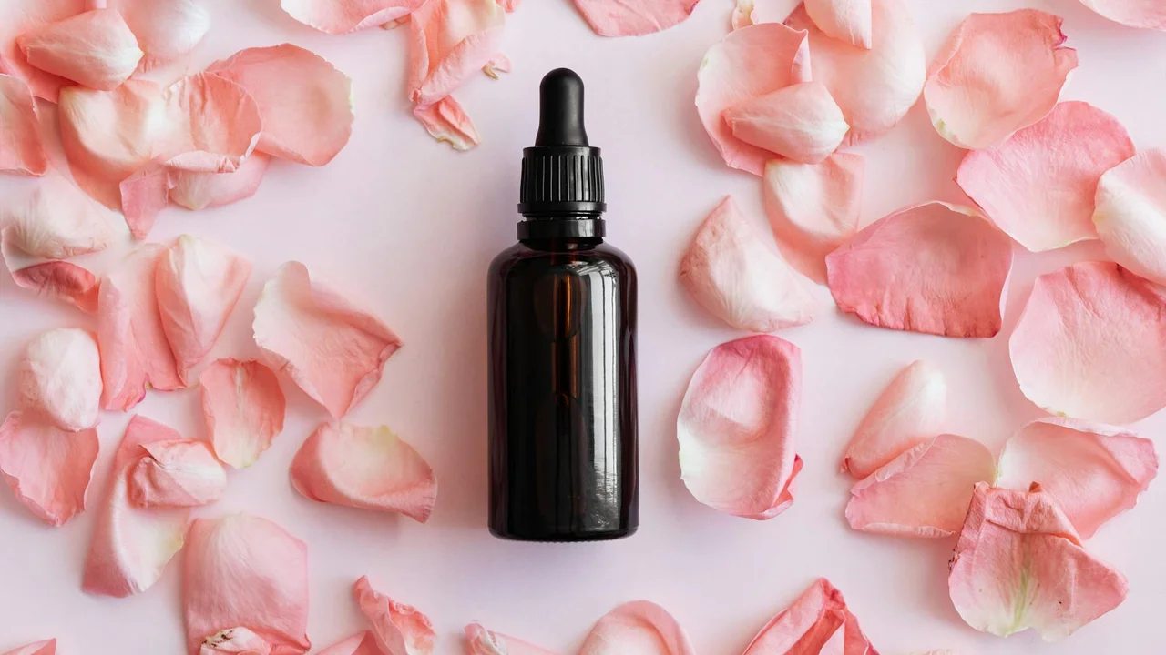 A dark glass dropper bottle sits on a light pink surface sprinkled with rose petals, illustrating coconut oil as a natural, whole-plant source of MCTs.