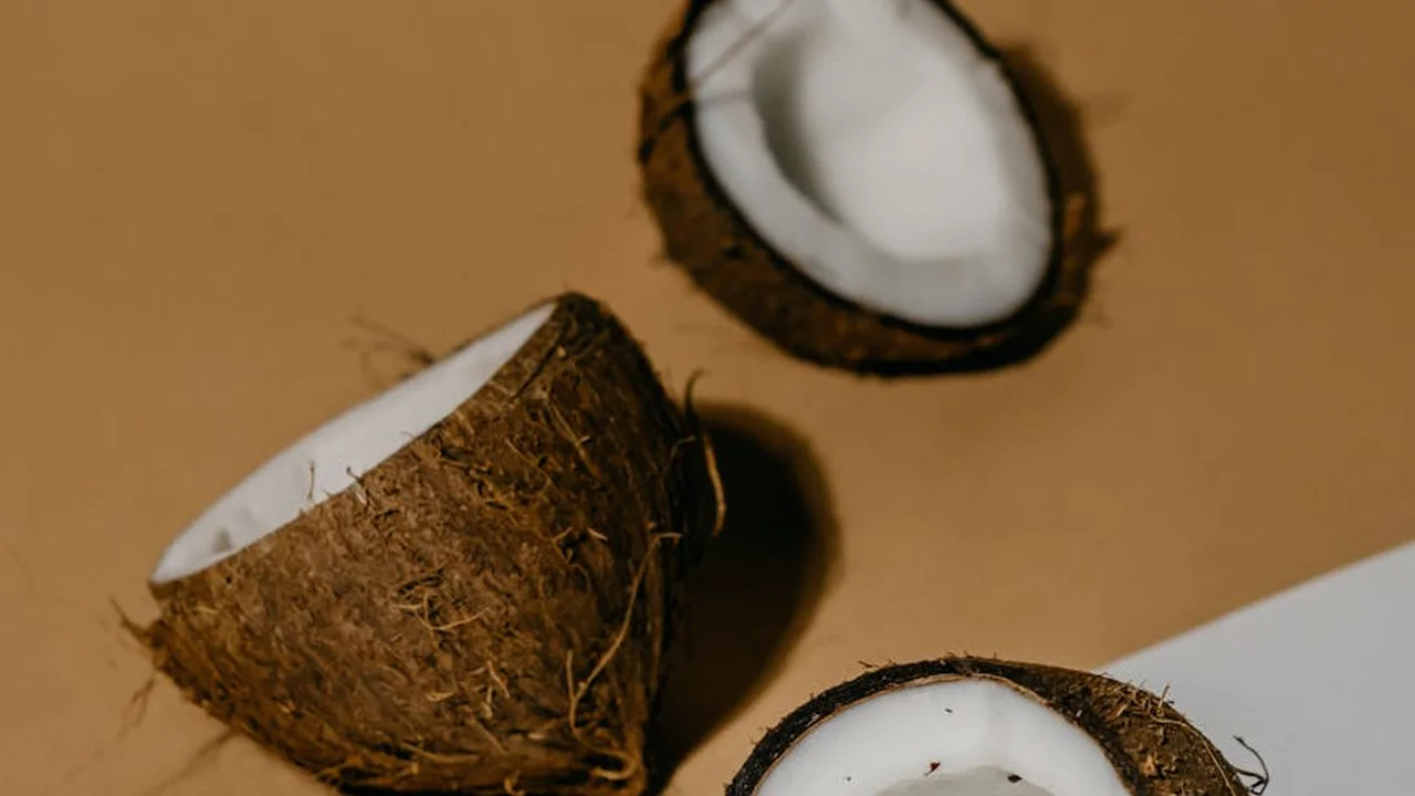 Two brown coconuts, one cracked open to reveal white coconut flesh, on a light tan background