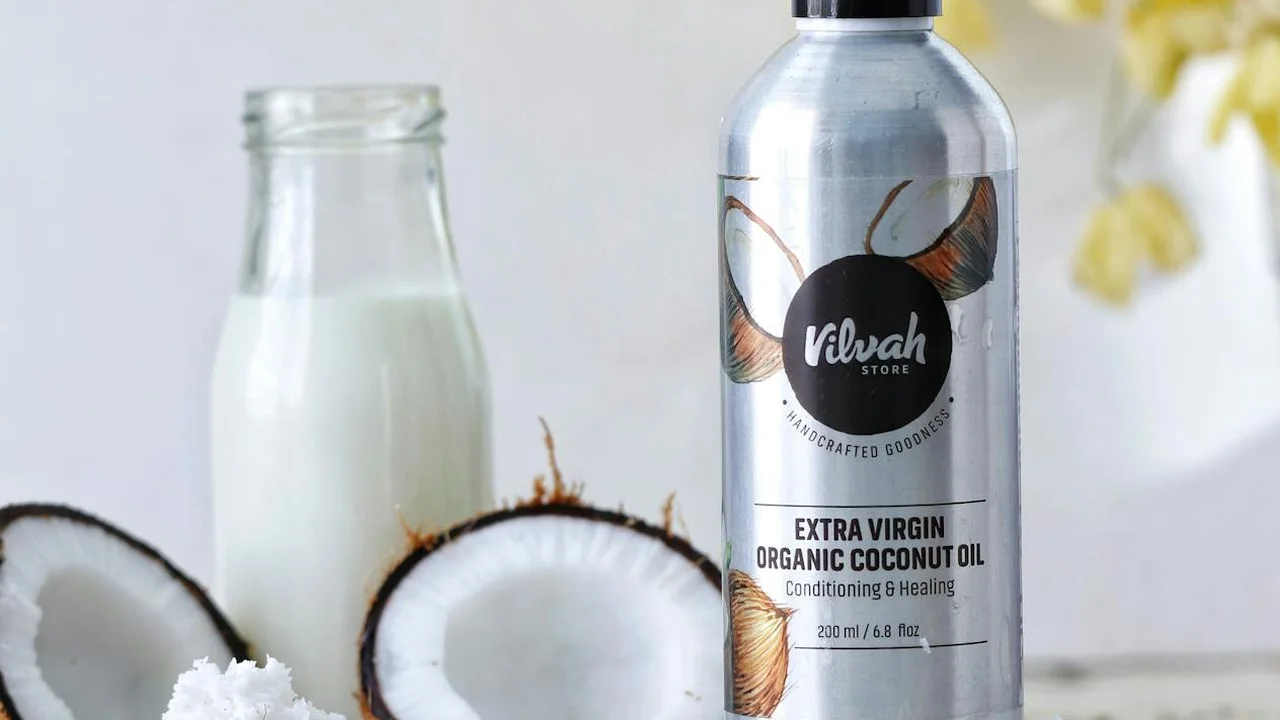 A bottle of extra virgin organic coconut oil beside a glass bottle of milk on a kitchen counter, with coconuts in the background.