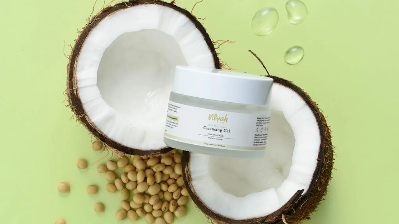 Coconut halves with a small jar of cleansing gel on a lime-green background, symbolizing integrating natural oil-based practices into daily routines.