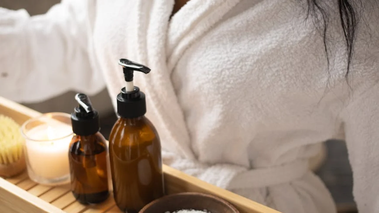 Person in a white robe sits beside a tray of skincare oils and a candle, illustrating natural skin and hair care substitutes.