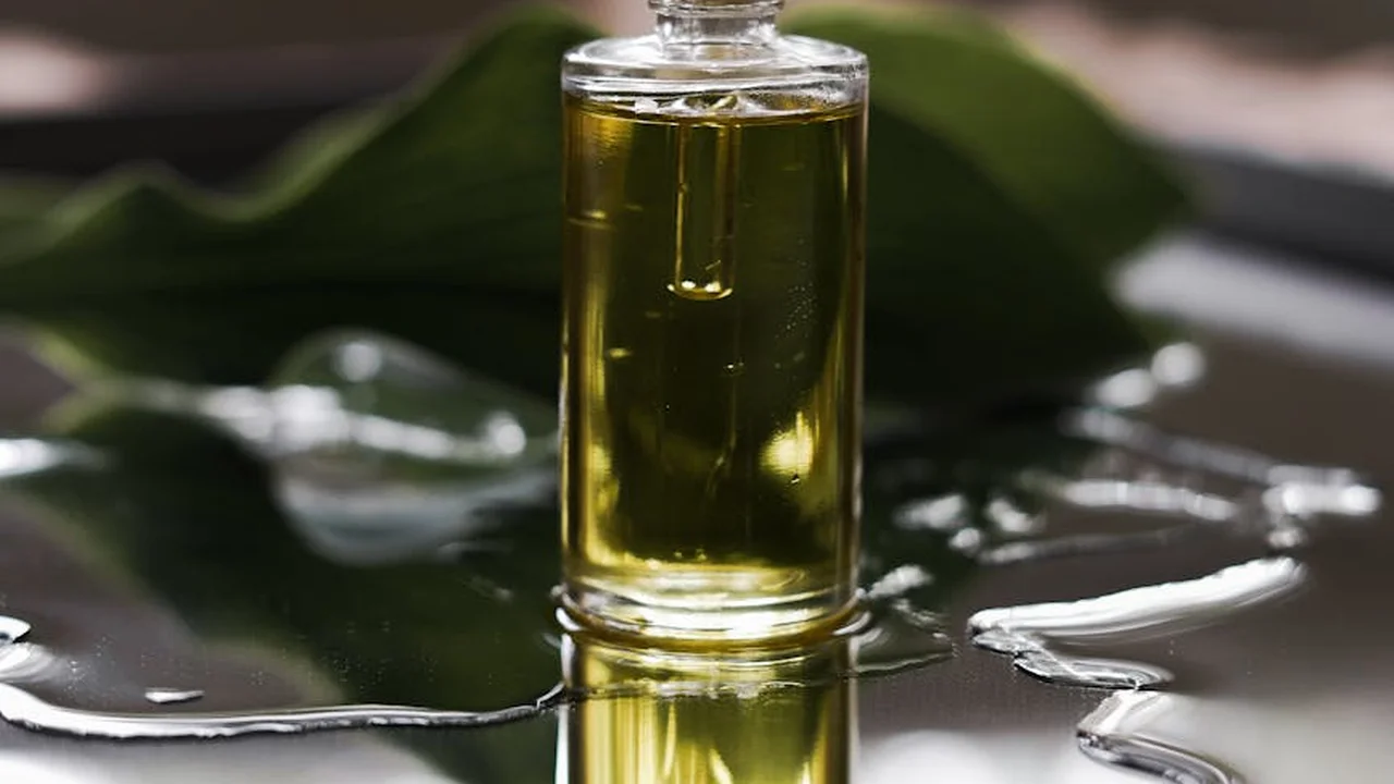 Glass bottle of golden oil on a dark surface with green leaves in the background