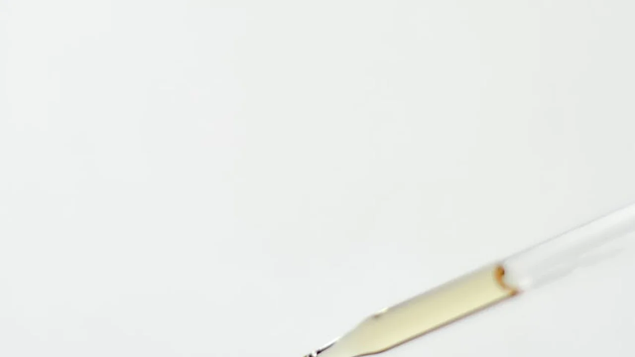 Close-up of a glass dropper with oil against a white background