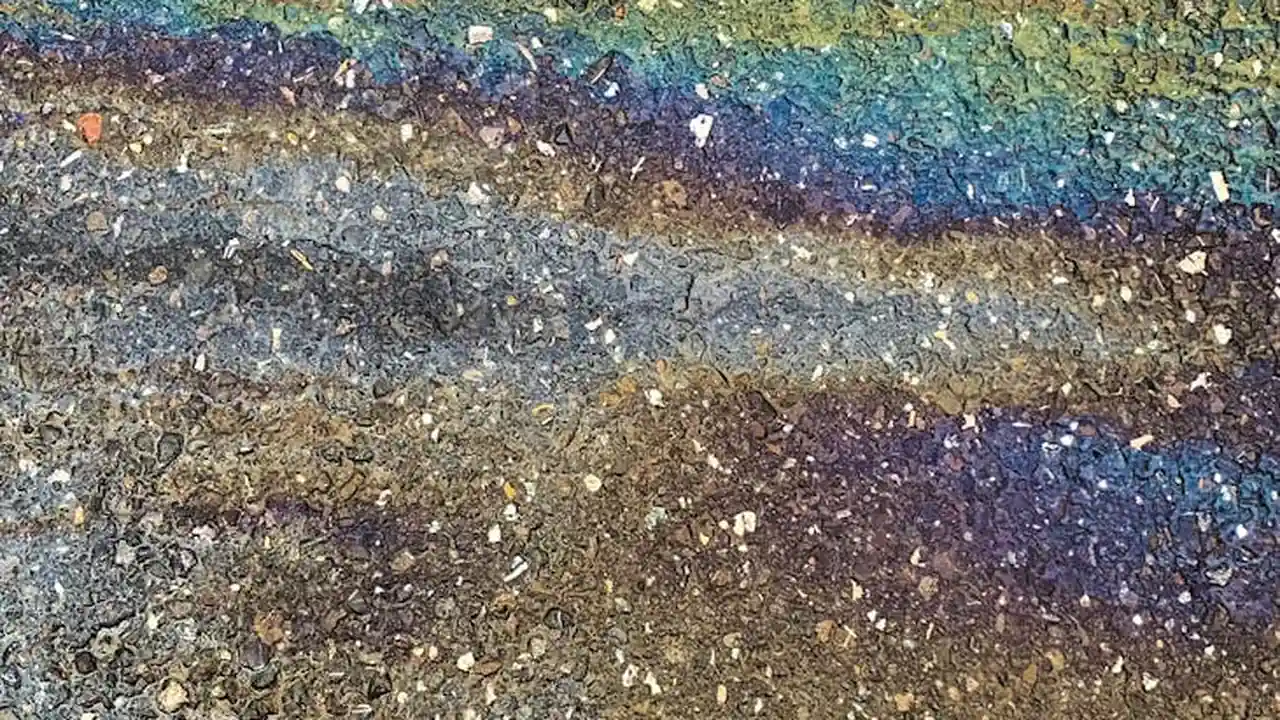 Concrete driveway surface with oil stains and scattered colorful specks