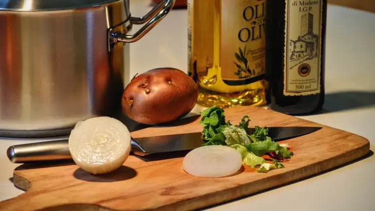 Cutting board with onion and knife, with bottles of olive oil in the background.